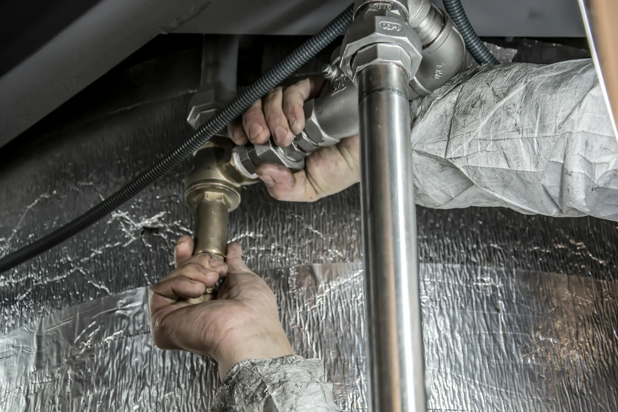 Plumber's hands fitting brass pipework under a kitchen unit in Bradford